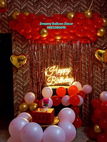 A cozy and intimate birthday setup at home. This decoration features a red balloon cloud, a rose gold fringe curtain, and a 'Happy Birthday' neon sign, perfect for smaller spaces.