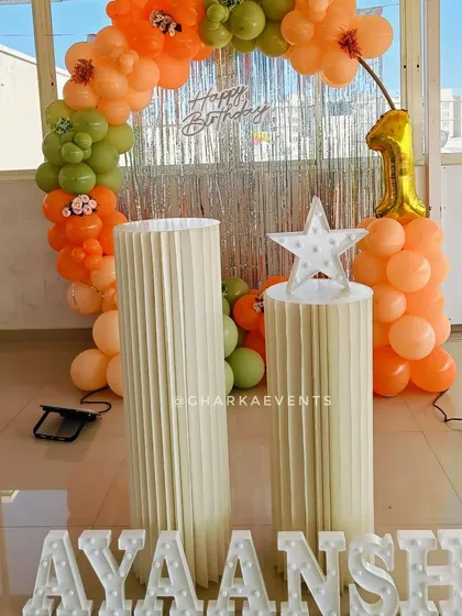 A detail shot of the decor for a first birthday. The combination of a silver tinsel curtain, an orange and green balloon arch, and a light-up star creates a festive and multi-layered look.