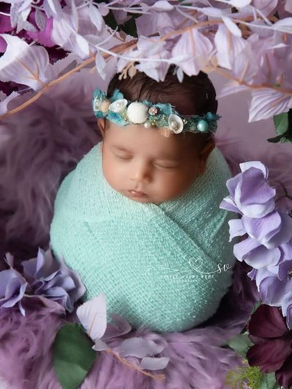 A beautiful, swaddled baby surrounded by a canopy of purple flowers. The lighting and colors give this portrait a very serene and dreamy quality.
