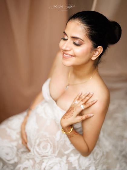 A close-up portrait capturing a moment of quiet joy. The delicate lace of the gown and the soft henna on her hand add beautiful, personal details.