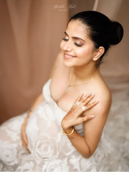 A close-up portrait capturing a moment of quiet joy. The delicate lace of the gown and the soft henna on her hand add beautiful, personal details.
