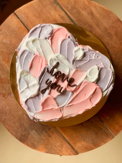 A heart-shaped cake with abstract pastel buttercream strokes and a simple "love you" message. This artistic design is modern and romantic.