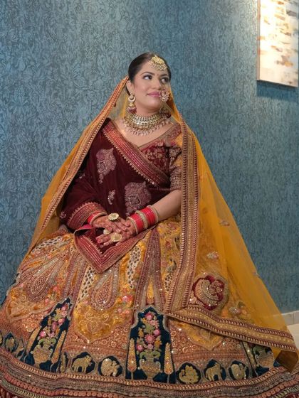 A seated portrait of a bride wearing our regal multi-panel velvet lehenga. This view highlights the rich colors and detailed embroidery on the skirt.