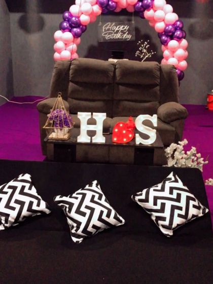 A simple yet beautiful birthday setup for an intimate celebration. This room features a pink and purple balloon arch over a comfy recliner, with marquee letters spelling out initials for a personal touch.