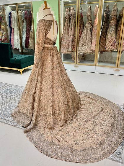 A back view of a stunning golden trail lehenga on a mannequin. The long, regal trail is covered in intricate embroidery, perfect for a grand entrance.