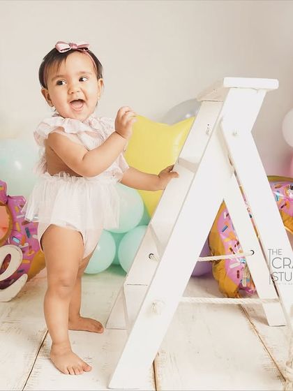 Standing tall and proud next to a prop ladder, this birthday girl is ready to climb and explore. A great shot showing off her new standing skills.