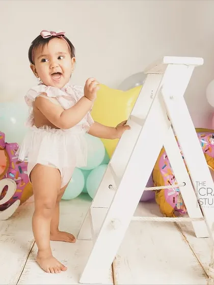 Standing tall and proud next to a prop ladder, this birthday girl is ready to climb and explore. A great shot showing off her new standing skills.