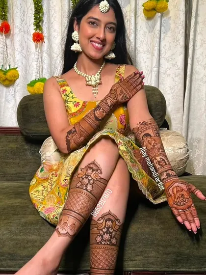 A stunning bride showing her full bridal mehndi on both arms and legs, all beautifully coordinated.