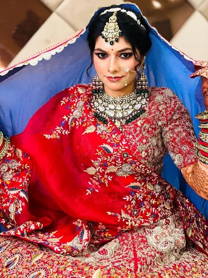 A regal bridal portrait. The bride lifts her blue dupatta, creating a beautiful frame for her face and showcasing her confident smile and flawless makeup.