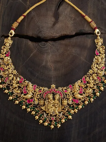 This is a piece I am incredibly proud of, a true example of wearable art. It's a gold-toned temple necklace featuring an intricate depiction of Radha and Krishna, detailed with meenakari enamel in rich pink and green. This handmade choker is for those who appreciate divine motifs and exceptional craftsmanship in their traditional jewellery.