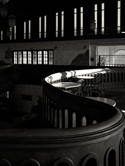 Sunlight filtering through the narrow upper windows creates stripes of light across the dark, curved balcony, highlighting its form.