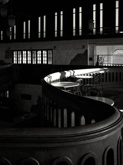 Sunlight filtering through the narrow upper windows creates stripes of light across the dark, curved balcony, highlighting its form.