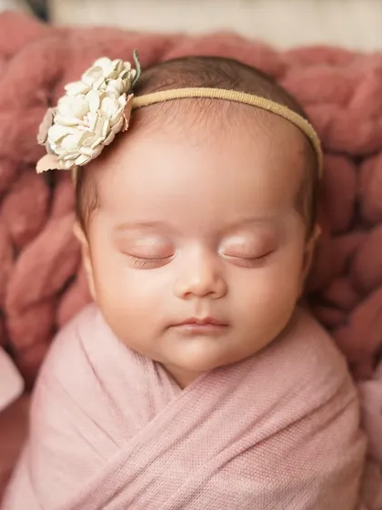 A tight close-up of the sleeping newborn's face, showing the delicate details of her floral headband and the soft texture of the wrap.
