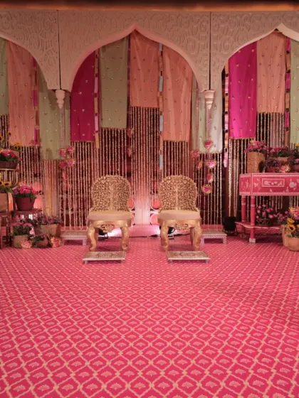 The main stage for the Mehendi ceremony, featuring a backdrop of pastel and rani pink drapes, ornate golden chairs, and an abundance of floral arrangements.