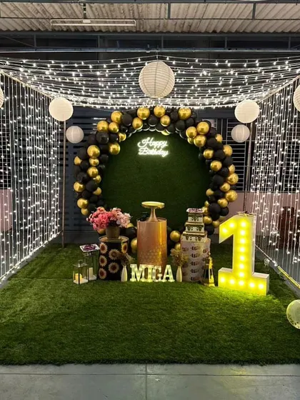 An enchanting outdoor birthday setup for a first birthday. We created a magical canopy of fairy lights and paper lanterns over an artificial grass patch, complete with a balloon ring and marquee number.