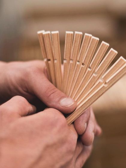 A close-up of a craftsperson's hands holding the precisely cut birch slats used to construct Secto Design lamps, emphasizing the quality of the material and the handmade nature of the product.