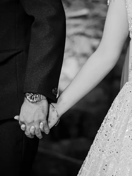 A close-up, black and white detail shot of a couple holding hands, a simple yet powerful symbol of their connection.