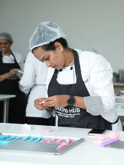 A student meticulously crafting small, delicate pink fondant decorations. This exercise hones fine motor skills and teaches the patience required for detailed cake artistry.