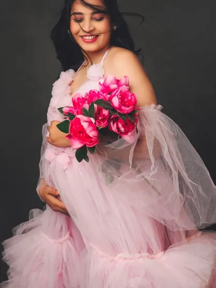 A happy and radiant mom-to-be in our pink floral-detailed tulle gown, holding a matching bouquet of peonies.