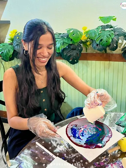 A participant smiles as she pours paint, fully engaged in the creative process at our fluid art event at a local cafe.