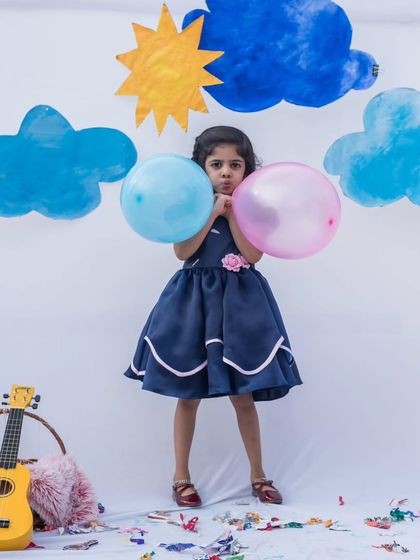 A playful and elegant navy blue dress for a fun-filled day. This shot captures the full silhouette against a whimsical backdrop, showing how comfortable and stylish it is for active little ones.