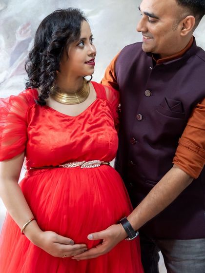 An intimate couple's portrait in the studio. The dad-to-be gently holds the baby bump, and they share a loving gaze against a soft, painted backdrop.