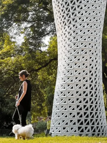 A candid moment showing the scale of the VERTO tower next to a person and their dog, illustrating its presence in a real-world park environment.