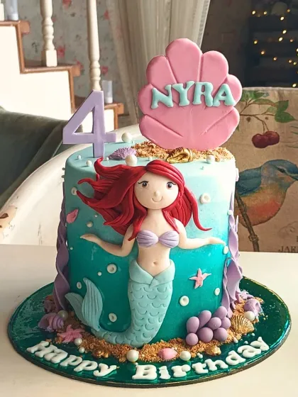 Dive into an underwater adventure with this Little Mermaid cake, showcasing a hand-sculpted Ariel, an ombre sea-blue finish, and delicate seashell details.