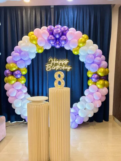 A simple yet elegant circular balloon arch in pastel purple, white, and gold. This setup includes a light-up number '8' and a 'Happy Birthday' neon sign, perfect for a stylish birthday party.