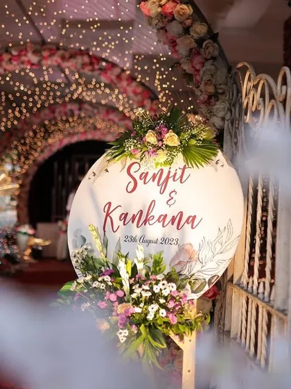 A personalized welcome sign for Sanjit and Kankana's wedding. The sign is set against a beautifully lit floral tunnel, creating a warm and personal greeting for guests as they arrive.