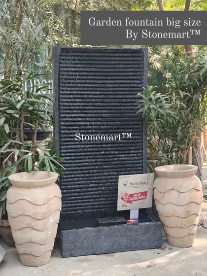 A large 5-foot granite garden fountain, flanked by decorative stone vases. This contemporary piece is fully chiseled by hand and adds life to any modern decor.