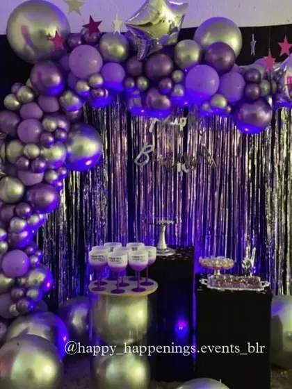 For this celebration, we went with a cool, futuristic vibe. A silver fringe curtain is the backdrop for a balloon arch in shades of metallic purple and silver, accented with star-shaped foil balloons for that extra pop.