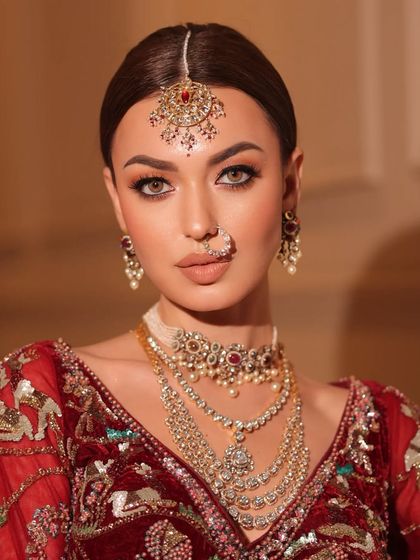 A close-up of a bride in a rich, maroon velvet lehenga. The styling includes a multi-layered diamond and ruby necklace for a truly regal feel.