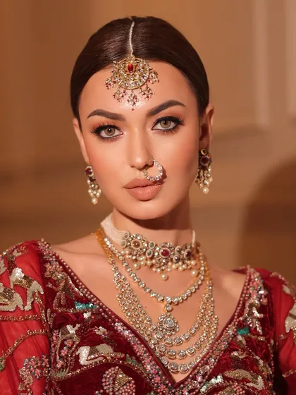 A close-up of the bride's radiant makeup and jewelry. The styling focuses on creating a flawless, glowing look that complements the rich red velvet.