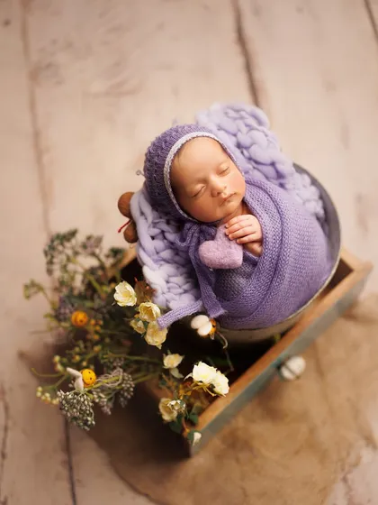I love combining different textures and props. Here, a chunky knit blanket, a rustic wooden drawer, and fresh flowers create a beautiful, whimsical scene for this sleeping baby.