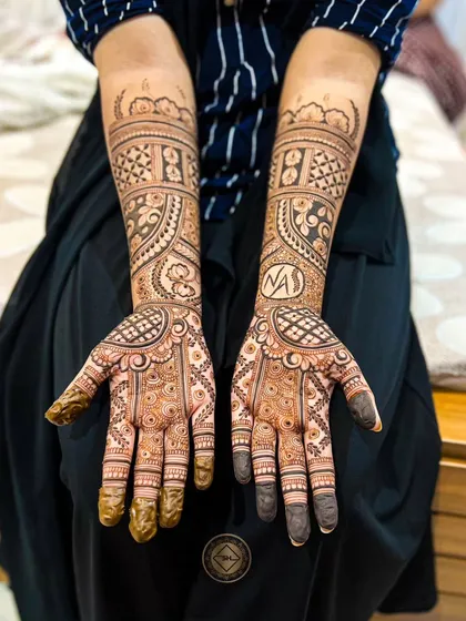For Neghla's bridal henna, we placed her and her partner's initials, N and A, inside a clean circular frame on her wrist. This is a popular way to personalize your wedding mehendi.