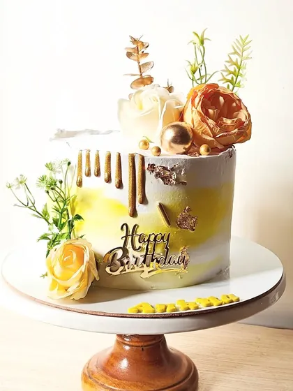A bright and sunny cake with a yellow watercolor effect, decorated with a gold drip, fresh flowers, and a "Happy Birthday" topper.