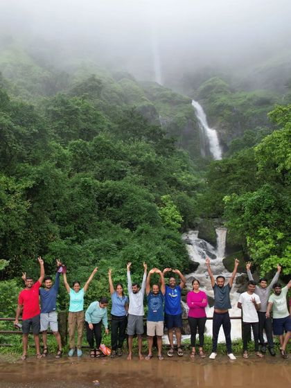 The group celebrates reaching a viewpoint with their hands up in the air, overlooking a valley filled with waterfalls.