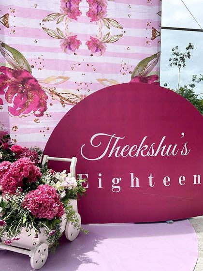 The personalized sign for Theeksha's eighteenth birthday, featuring elegant script against a rich magenta background, complemented by a cart of fresh flowers.