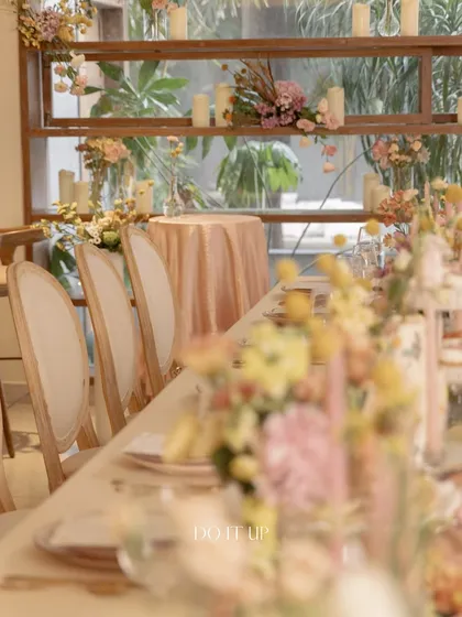 A dreamy anniversary brunch with a soft, romantic aesthetic. The long wooden table is adorned with a dusty rose runner, delicate florals, and elegant seating, creating a warm and inviting atmosphere for guests.
