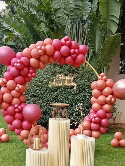 Celebrate your years together with a stylish anniversary decoration. This circular backdrop is adorned with a modern, organic-style balloon garland in shades of rose gold and pink, centered with a "Happy Anniversary" sign for the perfect photo opportunity.