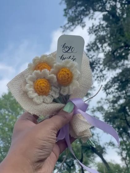The mini daisy bouquet held up against a background of green trees, looking fresh and cheerful.