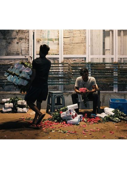 5:12am: Laborers at the flower market arrange bouquets of roses under the dim lights of early morning. The ground is scattered with petals, evidence of their hard work.