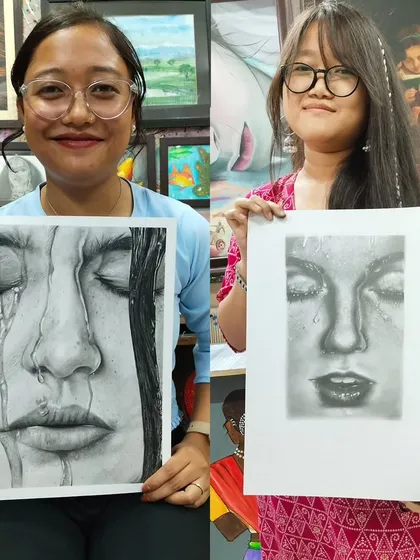 Two students proudly holding their hyper-realistic pencil portraits. It's amazing to see their progress and the incredible skill they develop.