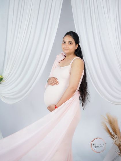 A side profile portrait that beautifully showcases the baby bump. The soft pink fabric flowing behind her adds a sense of movement and elegance.