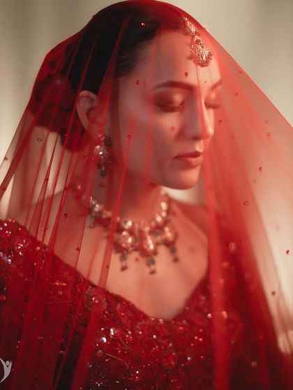 A dreamy, artistic shot of Simran through her red veil. The focus is on the mood and the beautiful color.