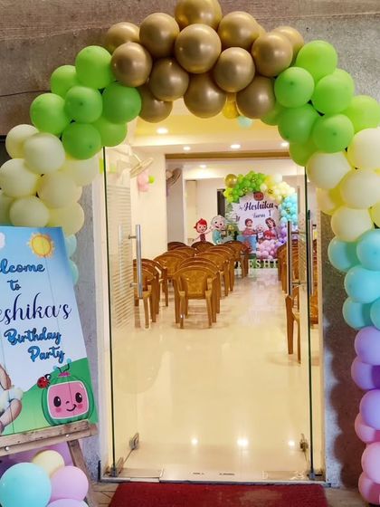 A welcoming entrance for a Cocomelon-themed first birthday, featuring a rainbow balloon arch and a personalized sign.
