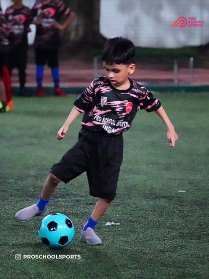 A young player dribbles with a bright blue ball, fully engaged in the training drill.