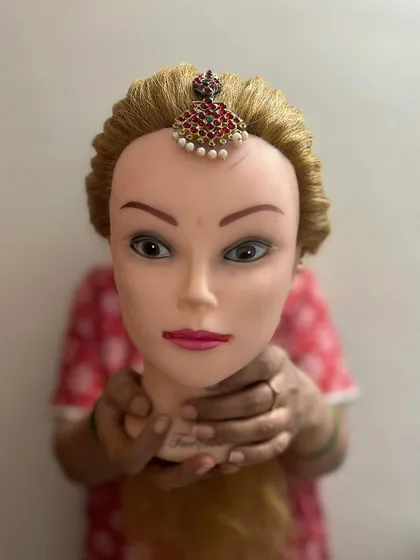 This image shows a student's hands holding the mannequin, demonstrating the hands-on nature of my classes as we work on precise accessory placement.