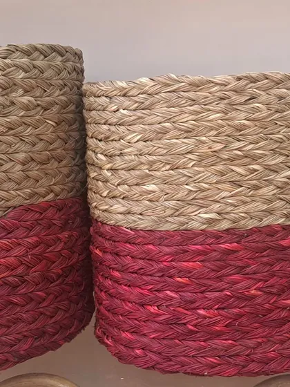 A pair of cylindrical baskets woven from natural seagrass and dyed a rich red on the bottom half. This two-tone design adds a pop of color, making them stylish decorative pieces or functional planters.